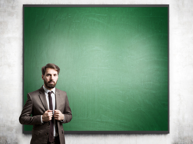 Businessman in suit with blackboard and concrete wall in the background. Mock up