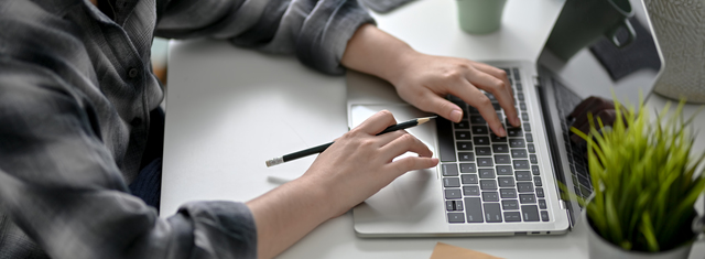 Cropped shot of female college student working with laptop and notepad at minimal worktable