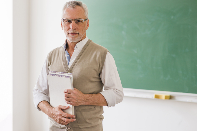 senior male professor glasses holding notebook standing against blackboard