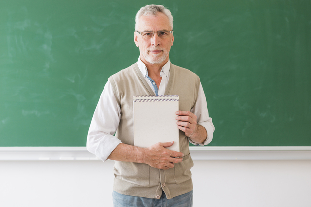 senior male professor holding notebook standing against blackboard 1